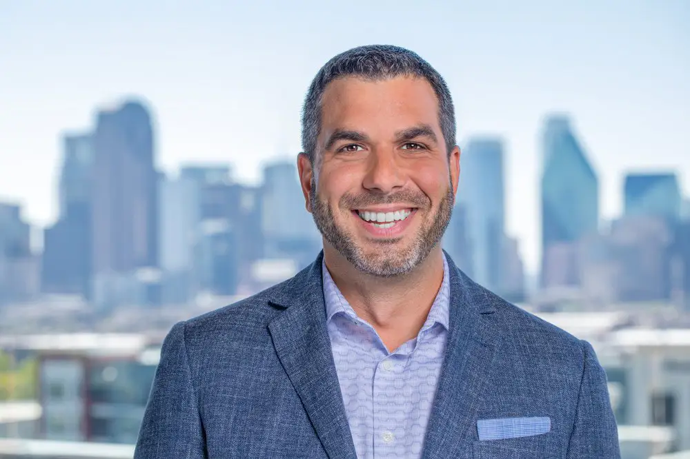 a man in a suit smiling in front of a cityscape