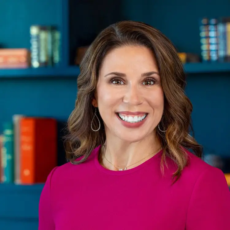 a smiling woman in a pink top in front of a bookshelf